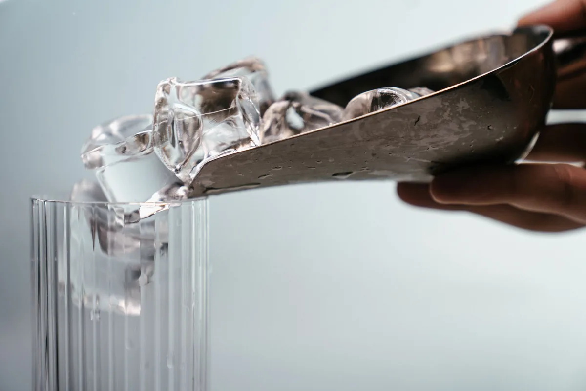 Una mano vierte hielo con una pala de acero en un vaso de cristal acanalado