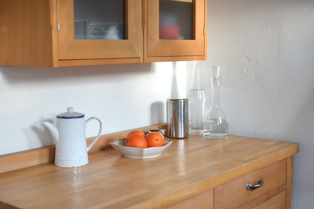 Encimera de madera de una cocina con una jarra blanca, un frutero con naranjas y dos jarras de cristal con agua