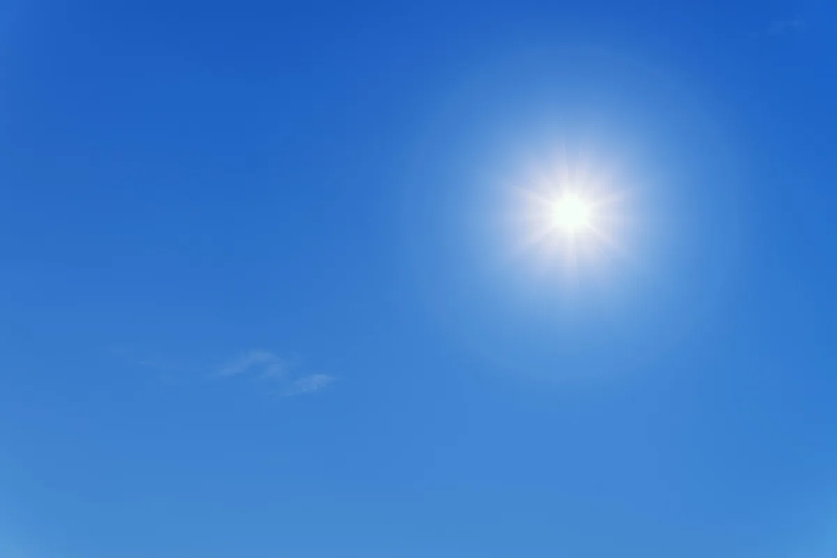 Sol brillante en un cielo azul despejado, con una nube fina abajo a la izquierda