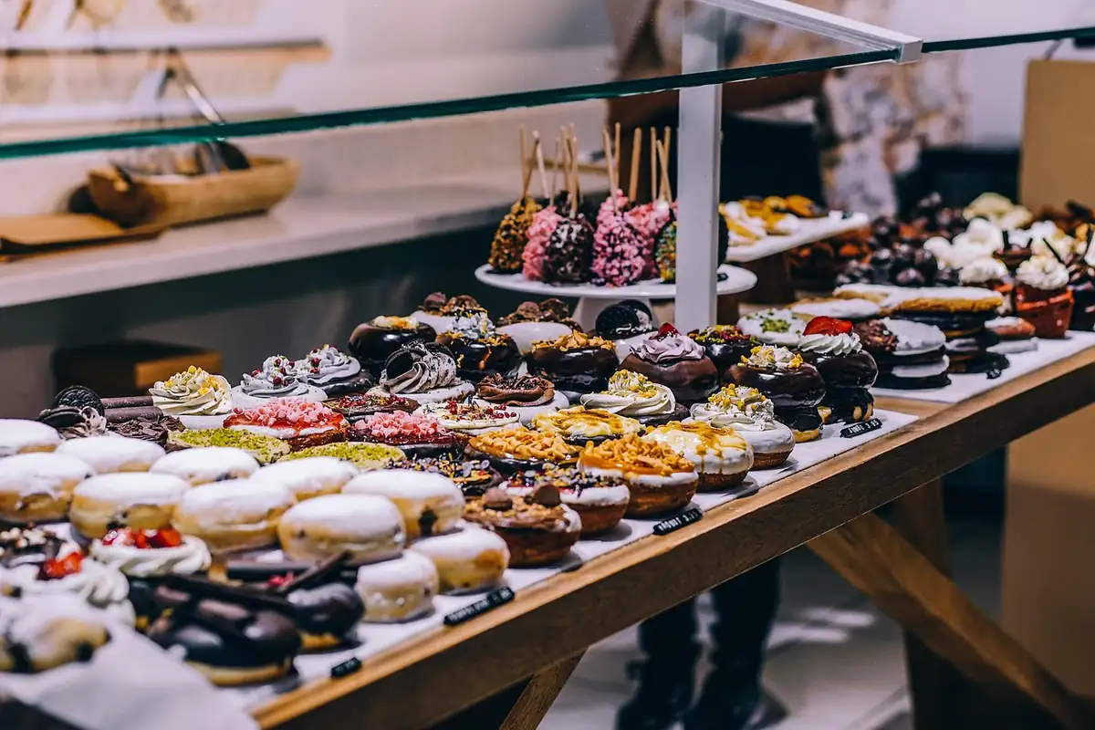 Expositor de cristal con donuts de varios sabores y coberturas sobre bandejas blancas, con etiquetas de precio negras