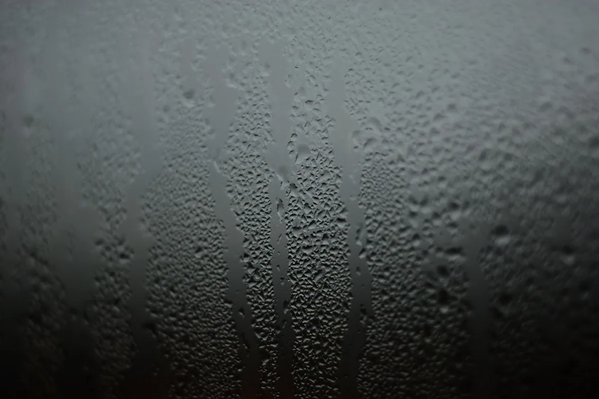 Gotas de condensación y regueros de agua sobre un cristal frío, en tonos grises
