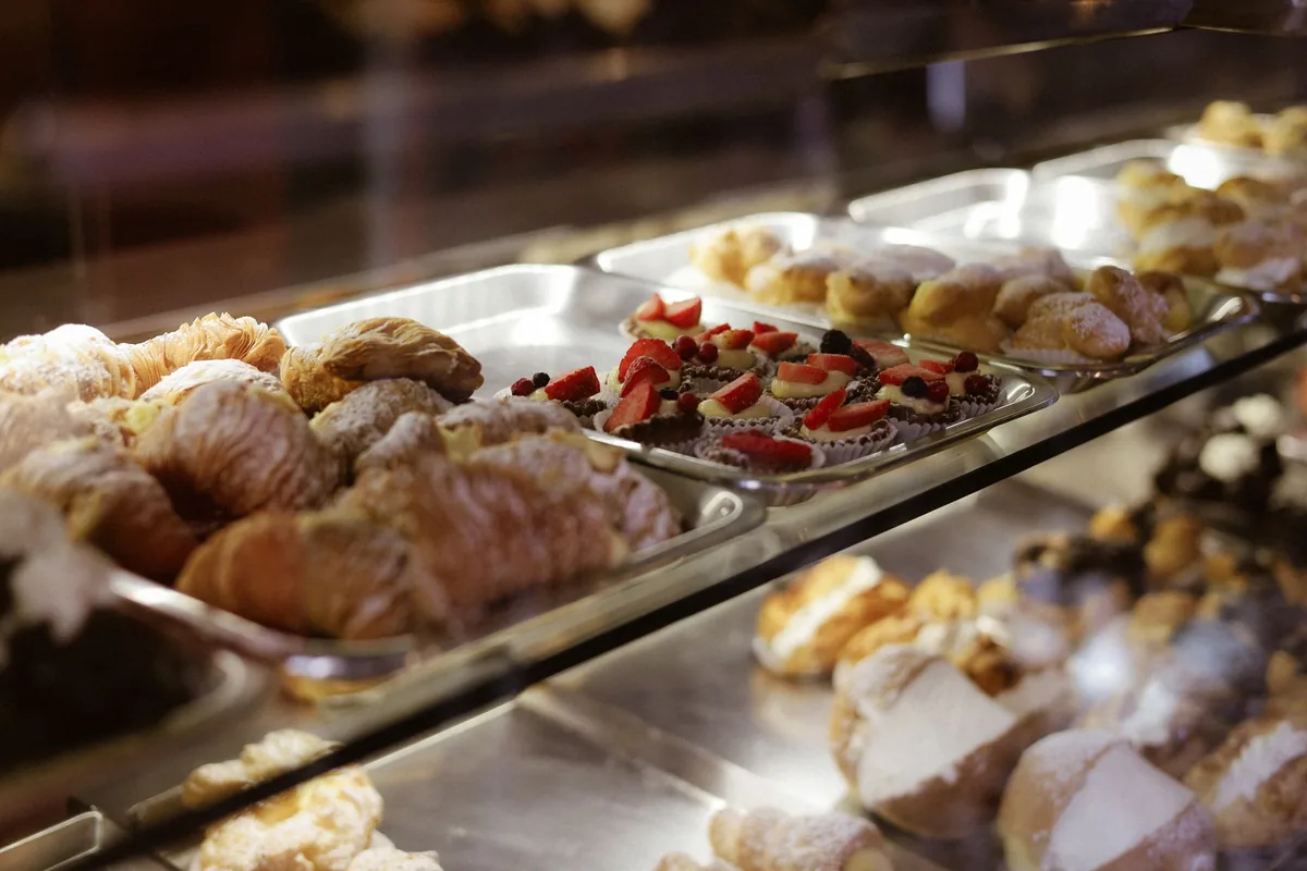 Vitrina de pastelería con bandejas de acero llenas de hojaldres, bollos y tartaletas con fresas